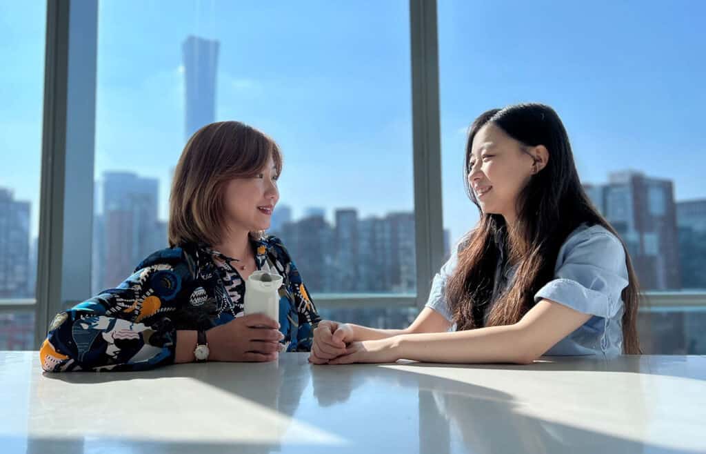 Two woman talking by a window city scape behind them | Bentley Systems | Infrastructure Engineering Software Company Two woman talking by a window city scape behind them