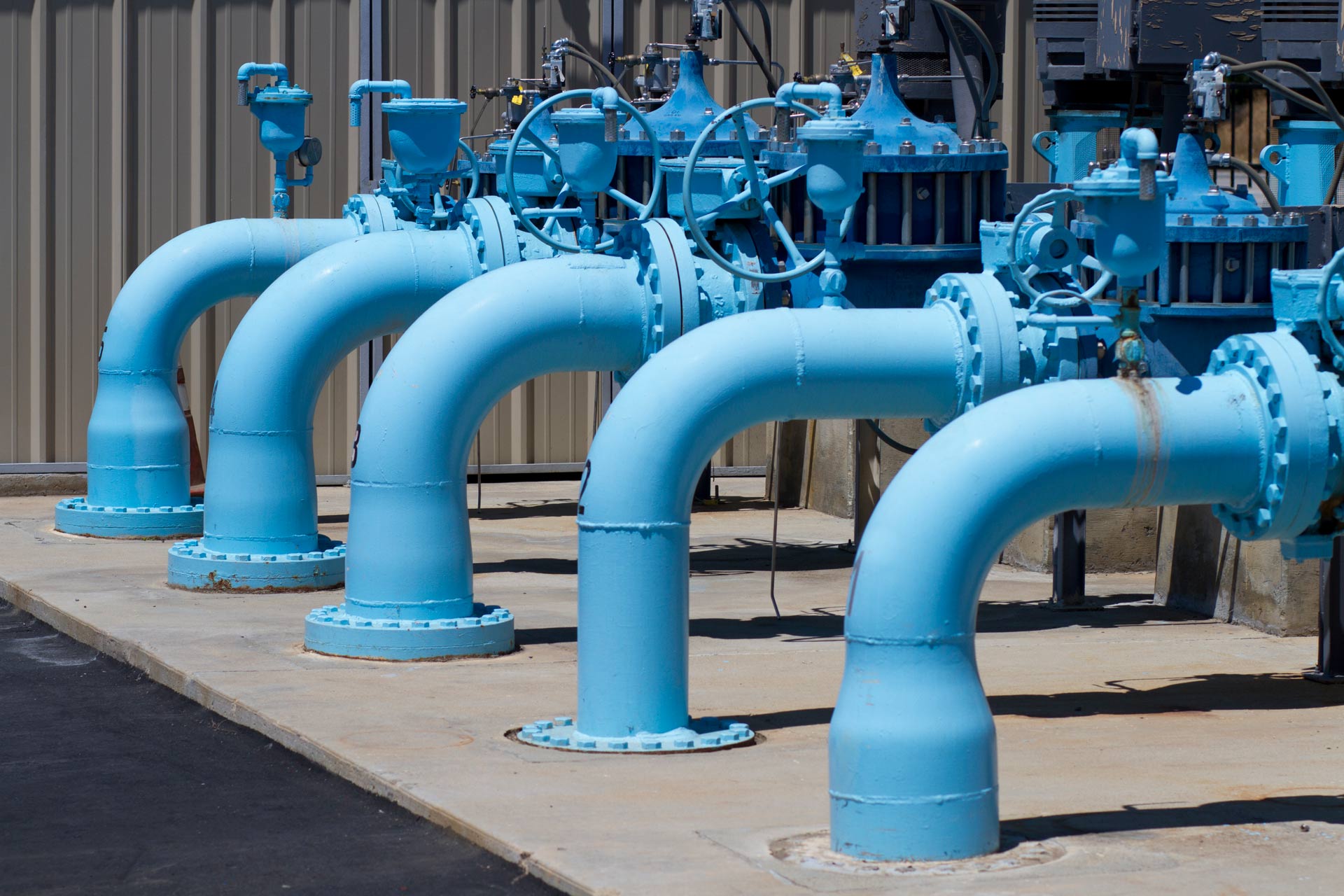 large blue water line pipes that are above ground and are going into the ground positioned outside a large building