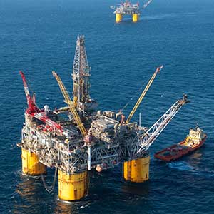 Offshore oil drilling platform in the ocean with a support vessel nearby.