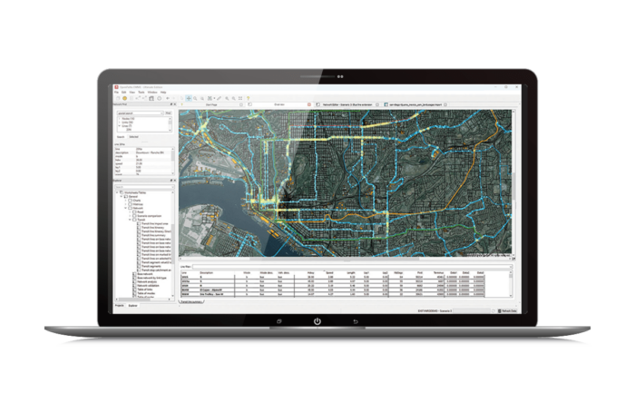 A laptop screen displaying a detailed geographic information system (GIS) map with various color-coded lines and data tables.